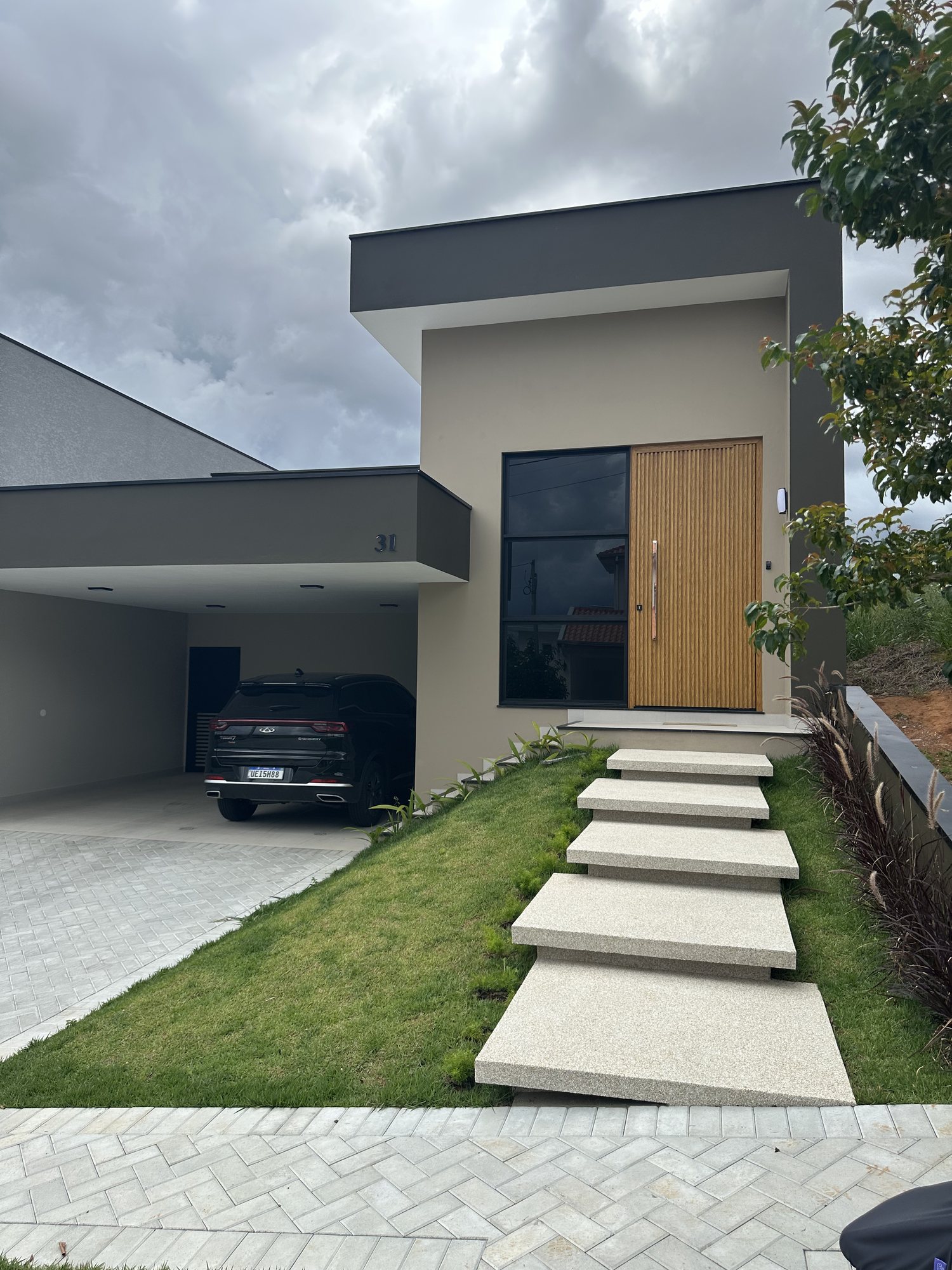 Fachada de casa de alto padrão em Bragança Paulista com porta pivotante ripada amadeirada e esquadrias pretas