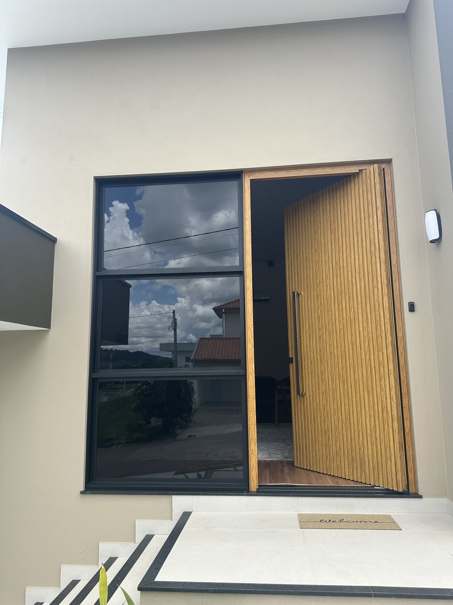 Porta pivotante ripada aberta mostrando o vão de entrada da casa em Bragança Paulista
